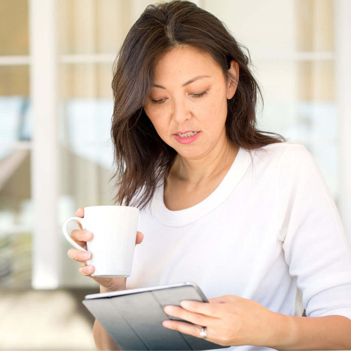 A woman drinking coffee outside while looking at her tablet